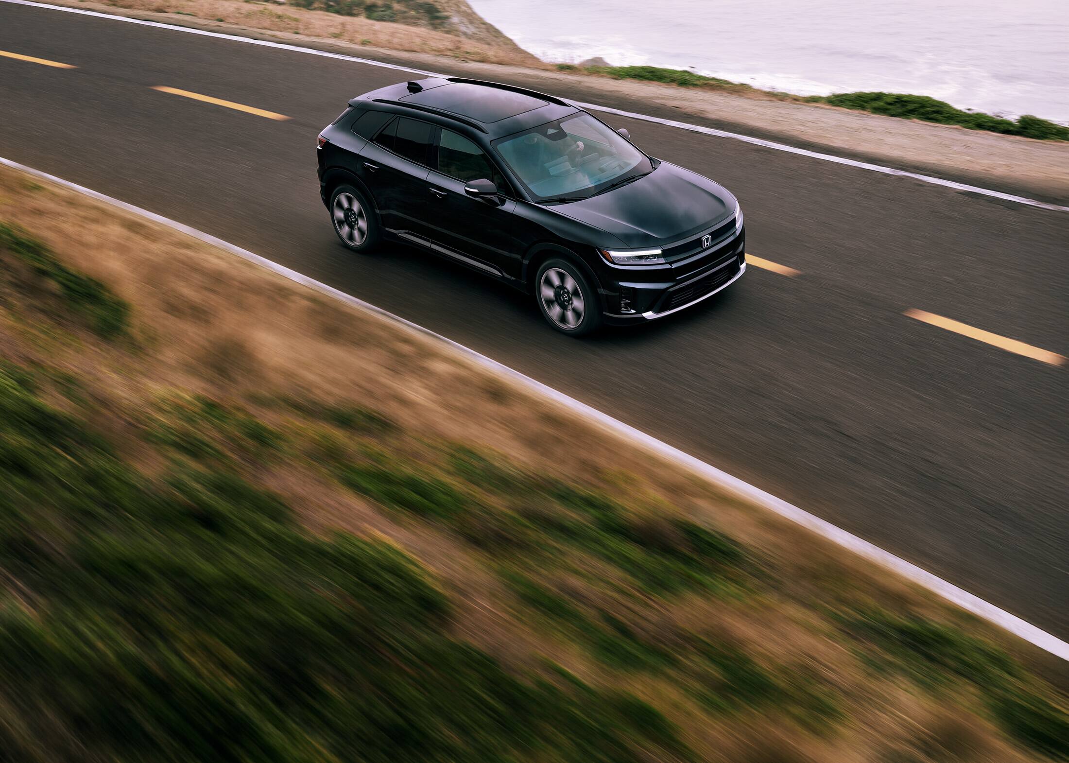 Front passenger view of the 2024 Honda Prologue Elite in Raven Black, shown driving along the coast.